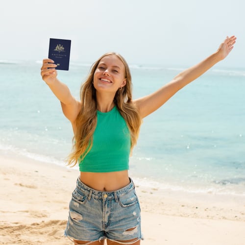 Happy tourist holding her Australian passport with visa for Indonesia inside while at the Beach in Bali