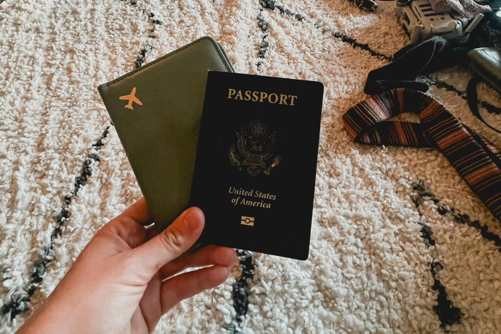 Рука, держащая паспорт США и дорожный блокнот на ковре, иллюстрирует время сбора документов.