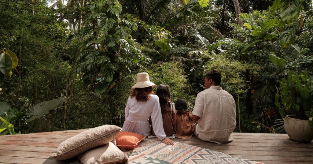 En familie sidder sammen på et trædæk i frodigt tropisk grønt og symboliserer sammenhold og starten på et nyt liv i Indonesien.