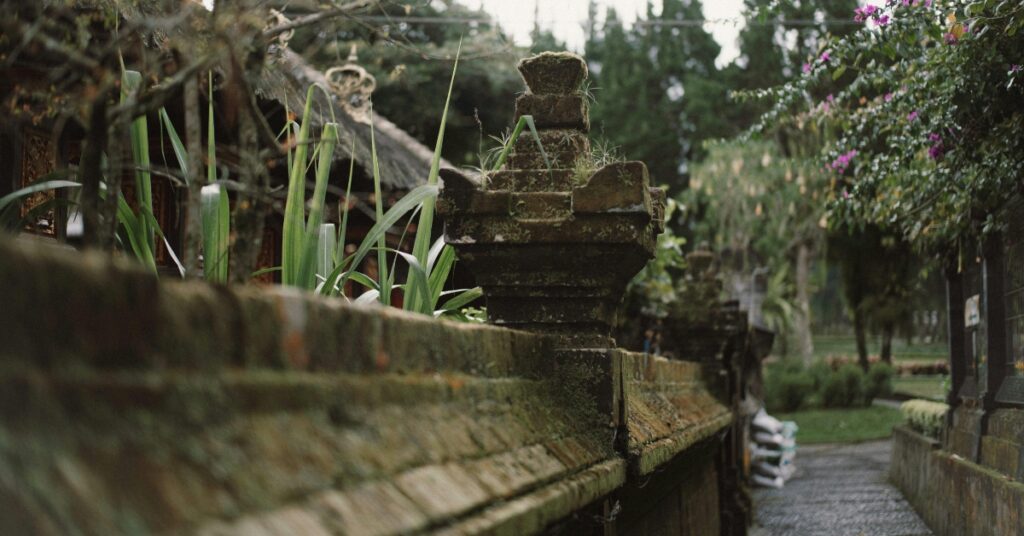 Stenen tempelmuur in Bali met bemost houtsnijwerk, tropische planten en een rustig pad, serene eilandomgeving voor digitale nomaden.