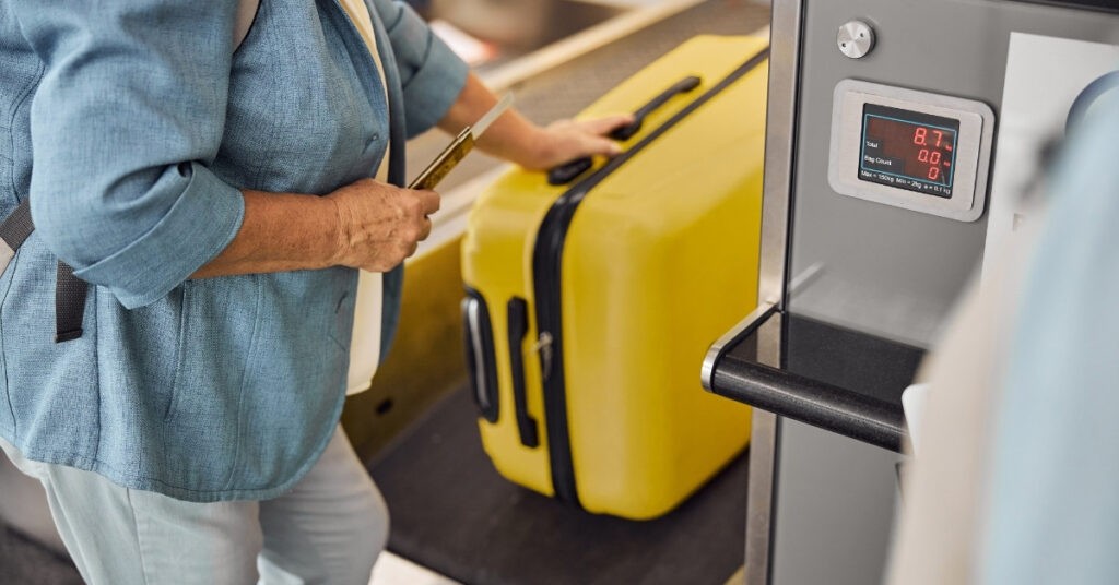 Traveler weighing a yellow suitcase at the check-in counter before departure.