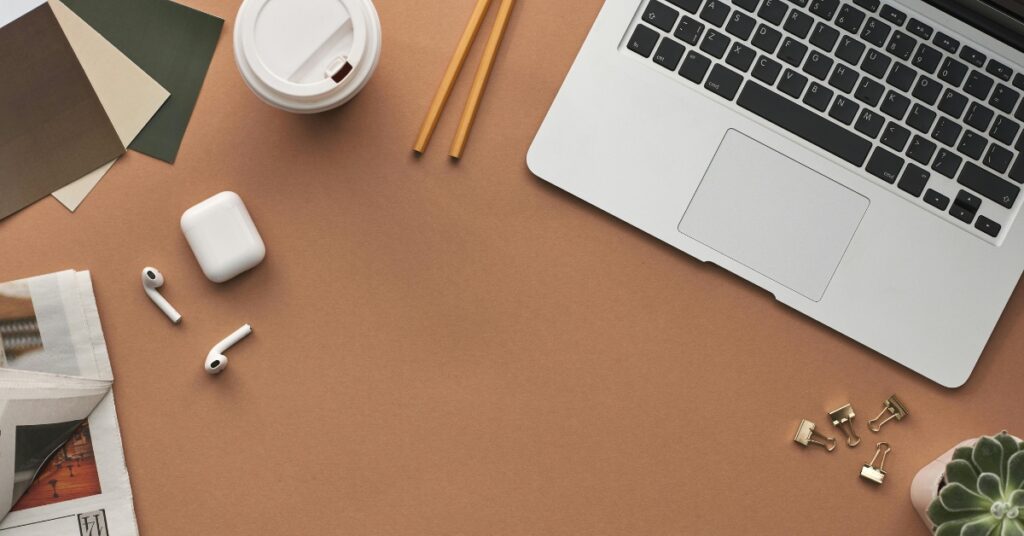 Minimaal bureau met laptop, koffiekopje, airpods, potloden en plant, schone digitale nomadenwerkplek in Bali.