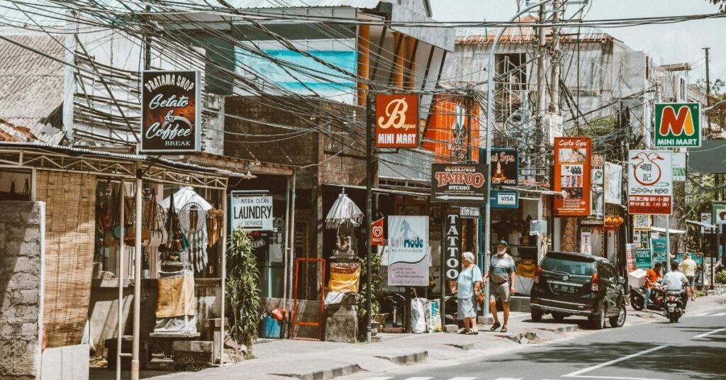 Жвава вулиця Балі з міні-маркетами, пральнями, тату-салонами та пунктами обміну грошей з барвистими вивісками.