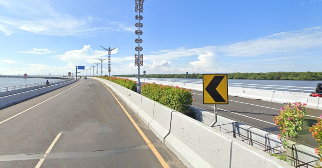 바다 위로 뻗은 발리 만다라 유료 도로의 전경과 자동차 차선 옆에 장식된 가로등 기둥, 꽃 칸막이, 오토바이 차선