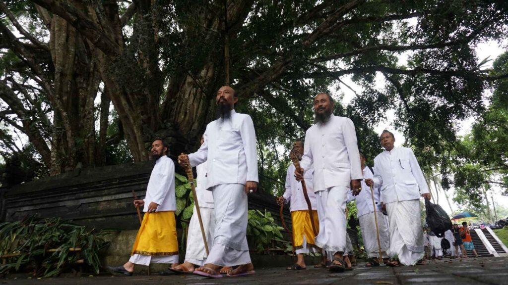 Balinese banjar members in traditional white clothing walking near a temple, representing local authorities involved in domicile letters.
