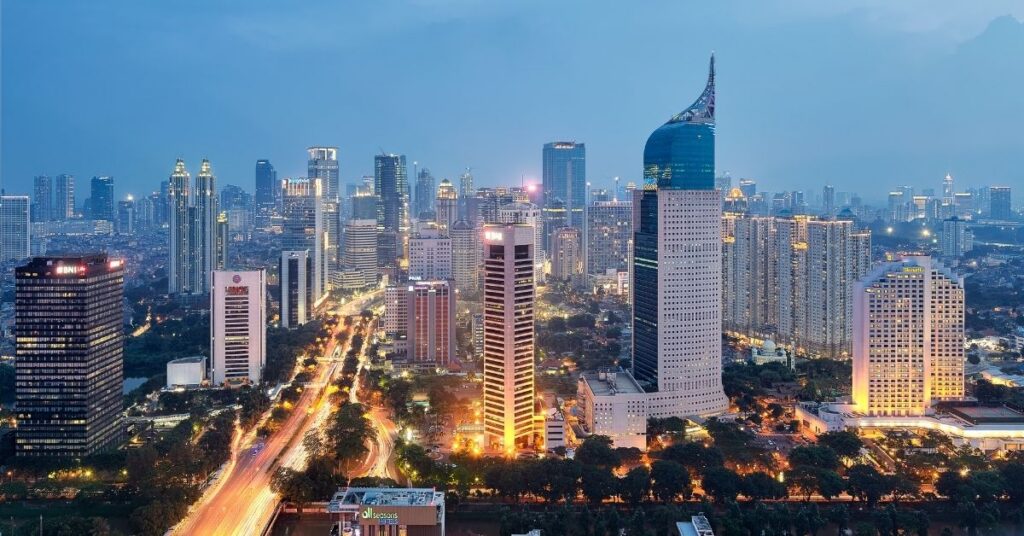 Jakarta skyline at dusk with high-rise buildings, busy roads, and glowing city lights.