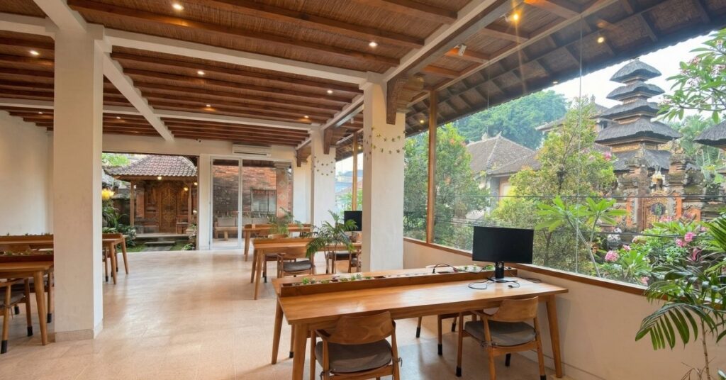 Open-air coworking space in ubud with wooden desks, tropical plants, and temple views.