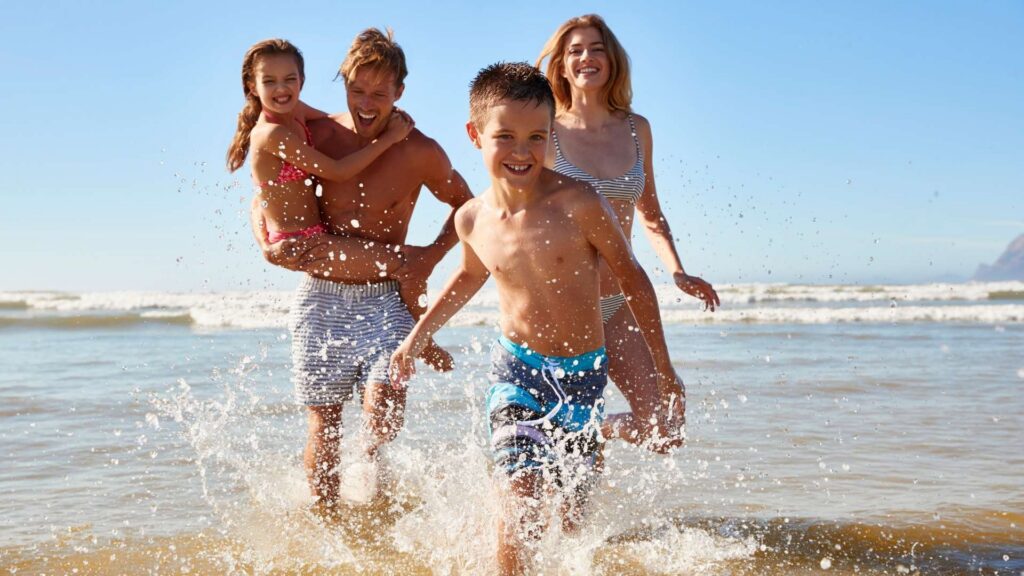 Family running through shallow ocean water at a sunny beach in bali