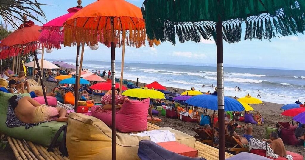 Canggu beach with colorful umbrellas and beanbags, lively surf scene and sunset bars.