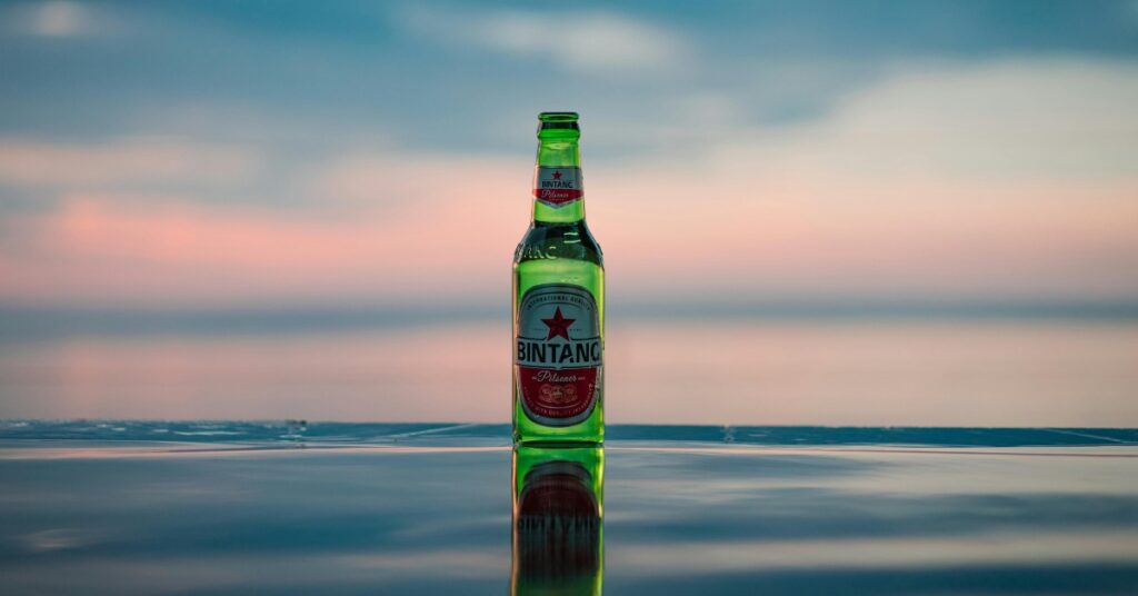 해질녘 해변가에서 시원한 빈탕 맥주를 마시며 현지에서 술을 사는 것과 발리에서 술을 가져오는 경험을 비교해 보세요.