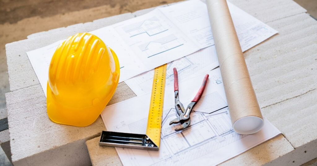Construction plans, measuring tools, and a yellow hard hat for an indonesia building permits guide