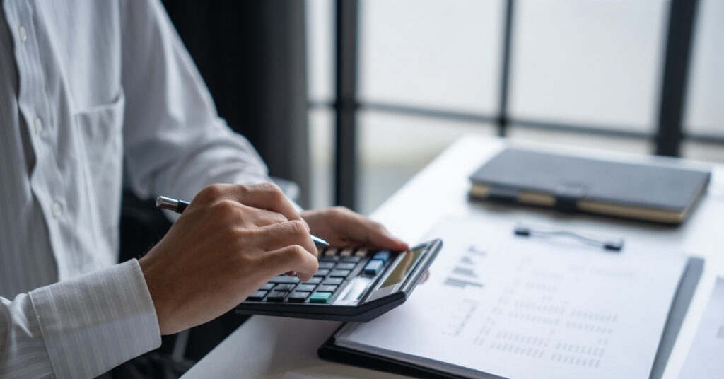 Business professional using a calculator and financial reports at a desk, calculating capital and compliance costs for doing business in indonesia.