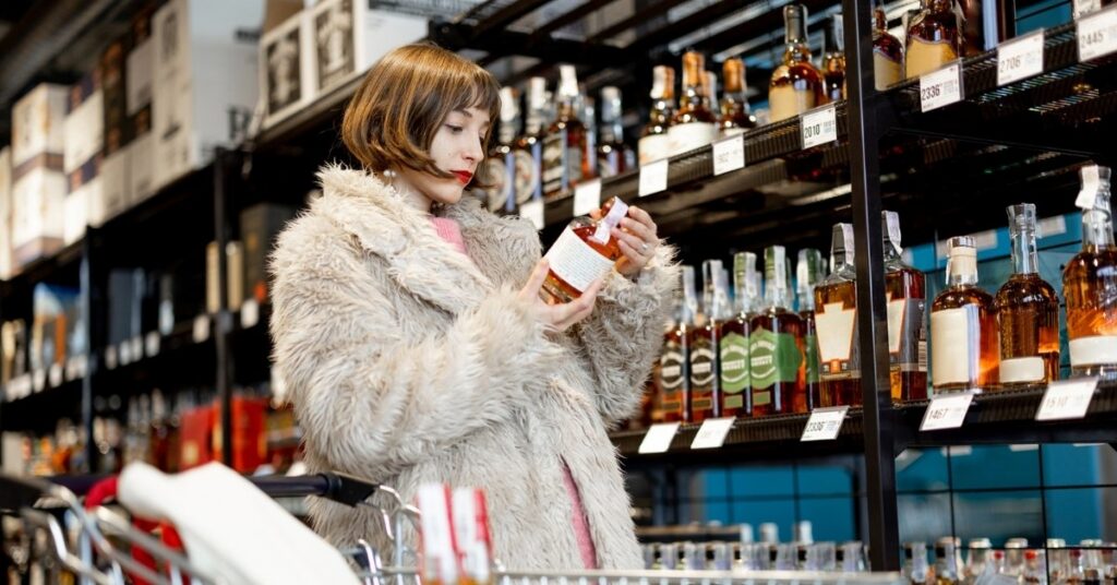 Shopper reading a whiskey label in a liquor store aisle, illustrating buying alcohol in indonesia and comparing alcoholic beverages.