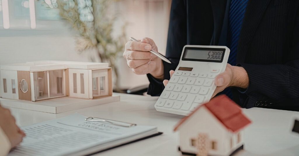 Person calculating property costs beside house models for indonesia building permits and land rights