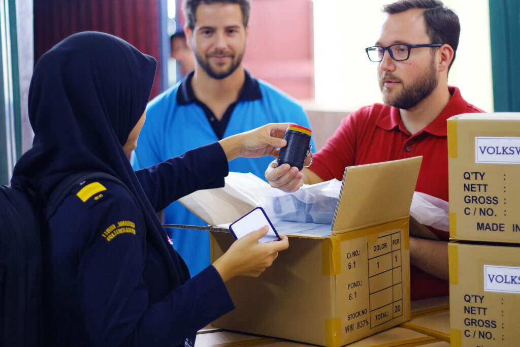 An indonesian customs officer inspecting a box during household import clearance with two foreign importers observing.