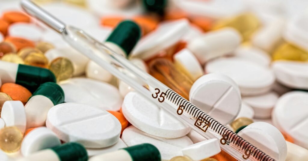 Крупный план различных рецептурных таблеток и капсул со стеклянным термометром, положенным сверху.