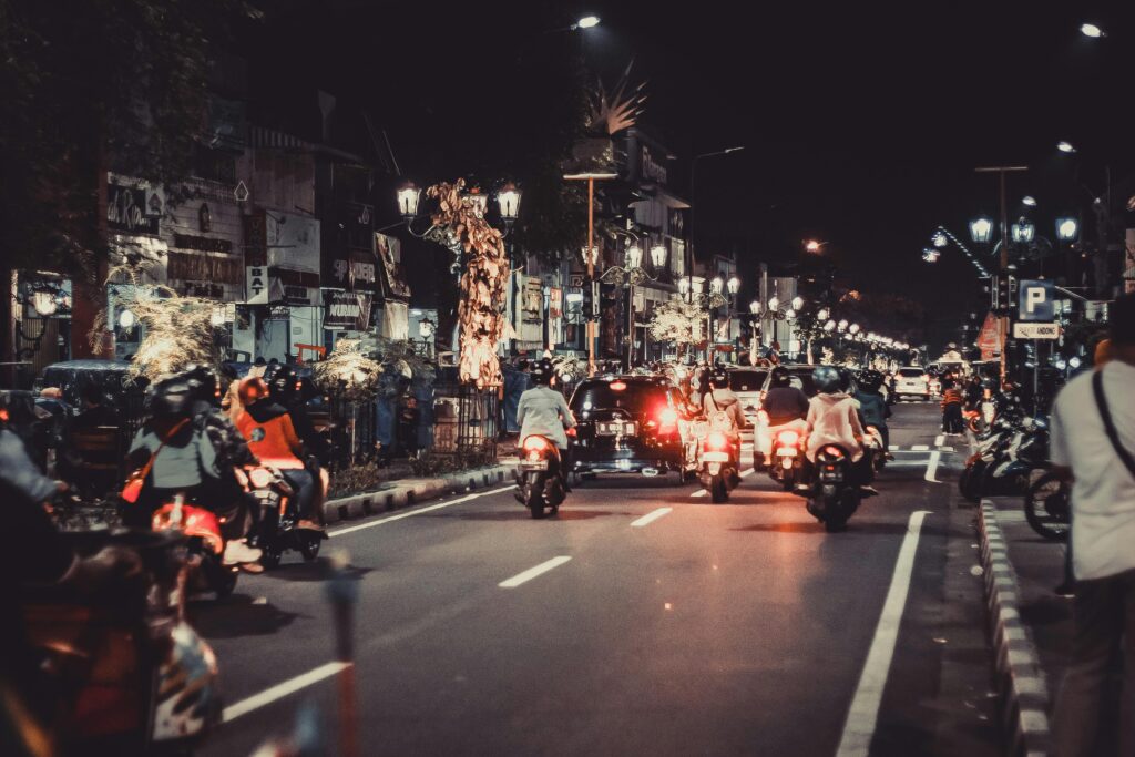 Nighttime traffic on a busy bali street with motorbikes and cars surrounded by shops and lights.