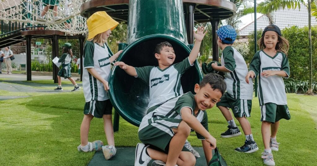 Young children in dyatmika school uniforms playing on a playground slide and grassy field in bali.