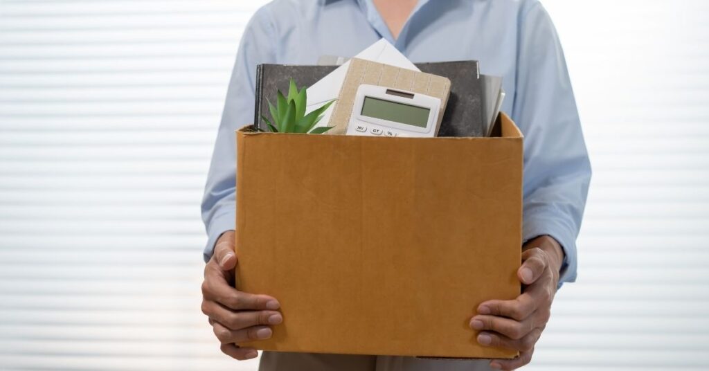 Business professional holding a box of personal belongings, symbolizing employee termination and offboarding.