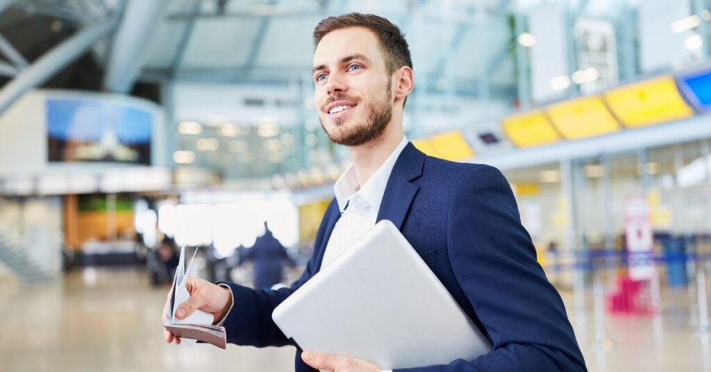 Viaggiatore d'affari sorridente in un aeroporto con in mano un computer portatile e documenti di viaggio, che rappresenta l'ingresso in Indonesia con un visto di pre-investimento.