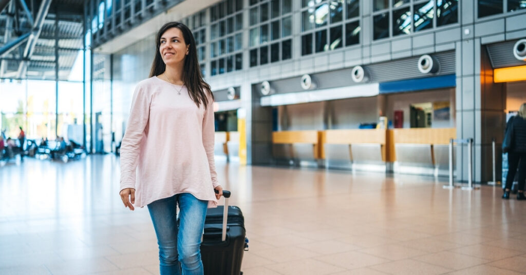 Woman walking through a modern airport terminal pulling a suitcase, looking ready for international travel.