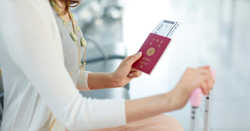 Traveler holding a japanese passport and boarding pass beside a suitcase handle, illustrating exit vs re-entry decisions before travel.