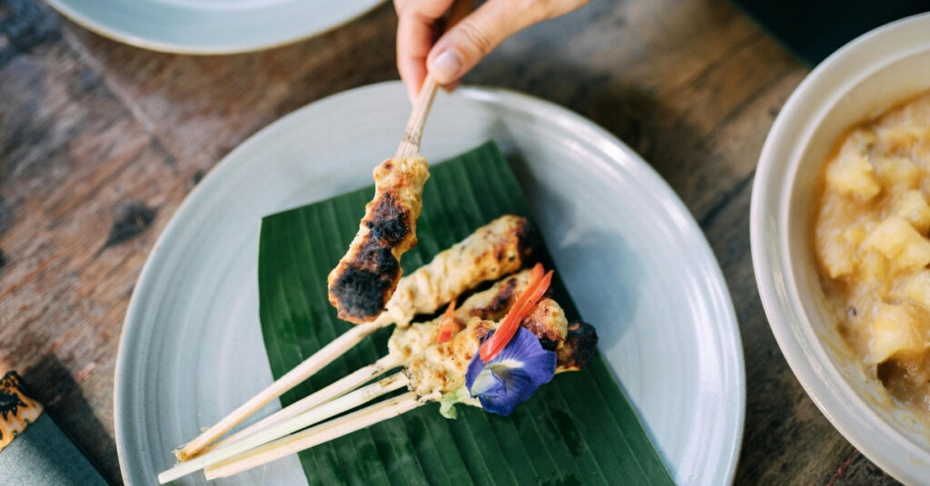 バナナの葉に盛られた伝統的なバリのサテの一皿で、新鮮な花が添えられている。