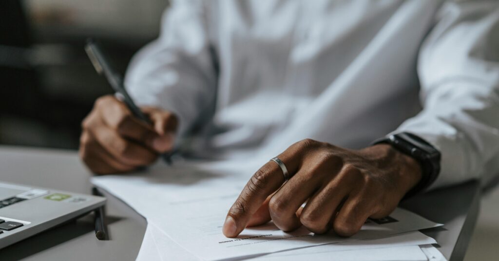 Primo piano di mani che compilano e firmano i moduli di iscrizione all'rptka accanto a un computer portatile.