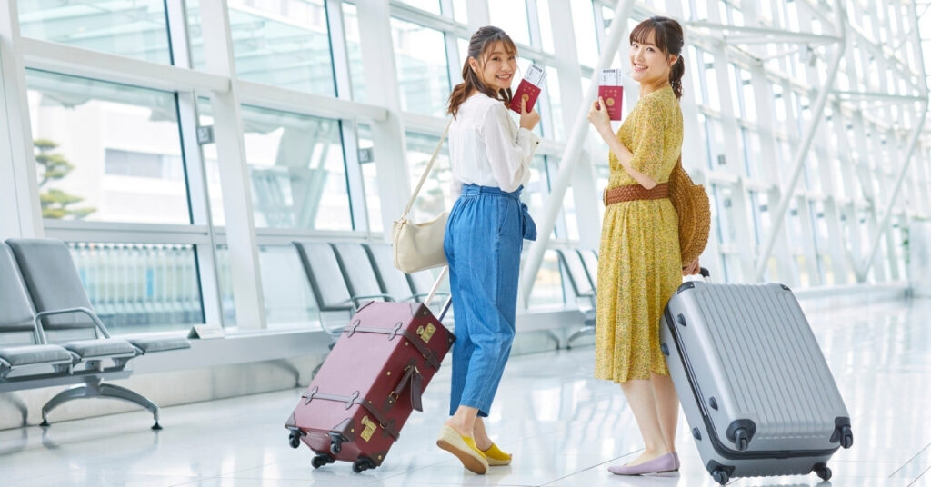 Two travelers smiling with passports and suitcases in a bright terminal, ready for check-in or self-transfer in Bali (DPS).