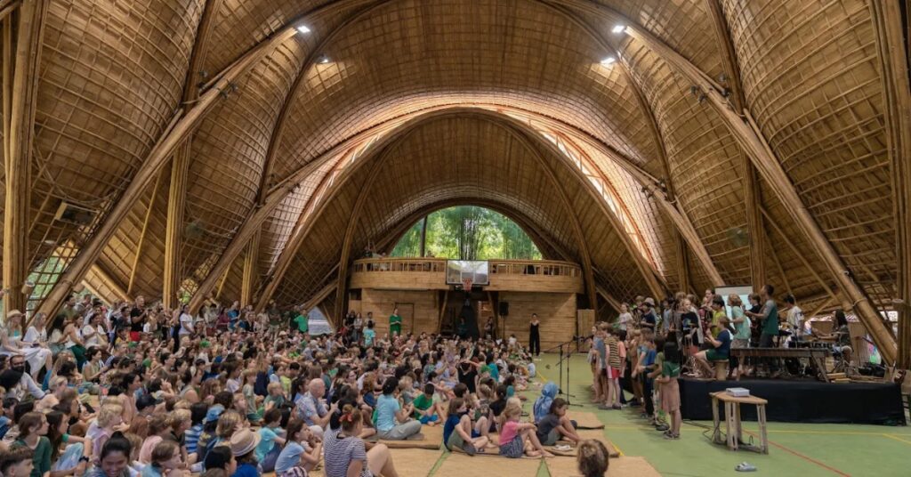 Large bamboo hall filled with students, parents, and teachers at green school bali, showcasing a community event in a unique eco-friendly campus.