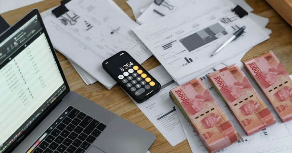 Ноутбук, документи, калькулятор і пачки індонезійських рупій на столі, що представляють собою розрахунок заробітної плати та сплату податків для іноземних працівників в Індонезії.