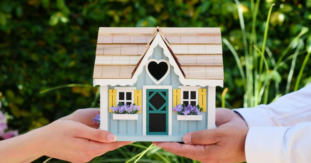 Руки тримають мініатюрний будиночок, що символізує варіанти оренди та власності в Балі.