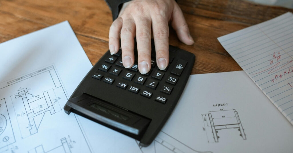 別荘の設計図の上で電卓を使う人。バリの別荘建築の予算とコスト計画を象徴している。