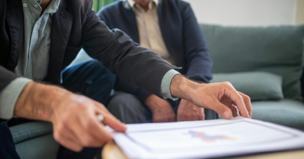 A man pointing at a printed insurance form during a discussion, representing the step-by-step process of buying travel insurance.