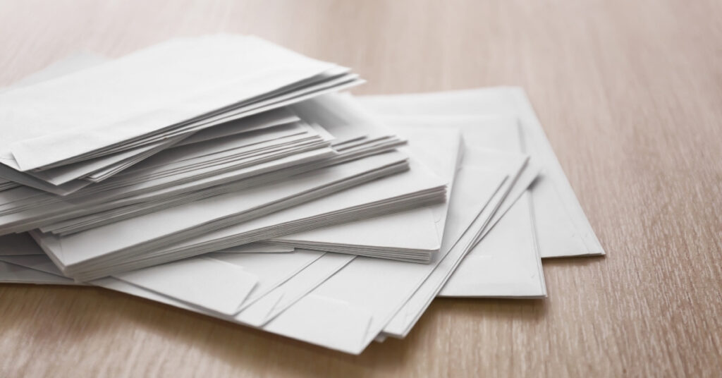 Stack of white envelopes on a wooden desk, representing incoming business mail and document handling for a virtual office.
