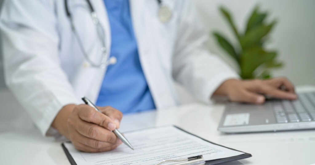 Врач заполняет медицинскую форму на планшете, используя ноутбук в клинике
