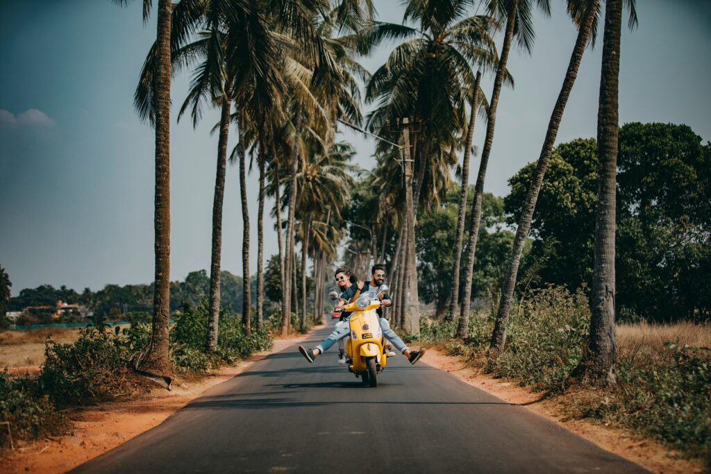 Dos personas montan en una scooter por una carretera tropical bordeada de palmeras, simbolizando la libertad de volver a entrar y explorar indonesia con el visado de negocios de entrada múltiple.