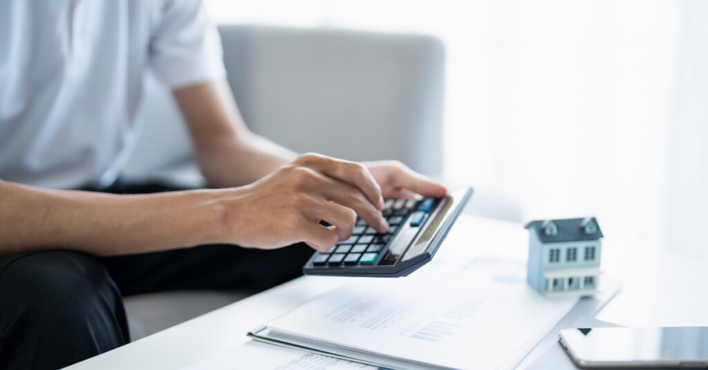Person using a calculator near a house model and documents, showing tax planning and residency concerns for tax for expats in indonesia.