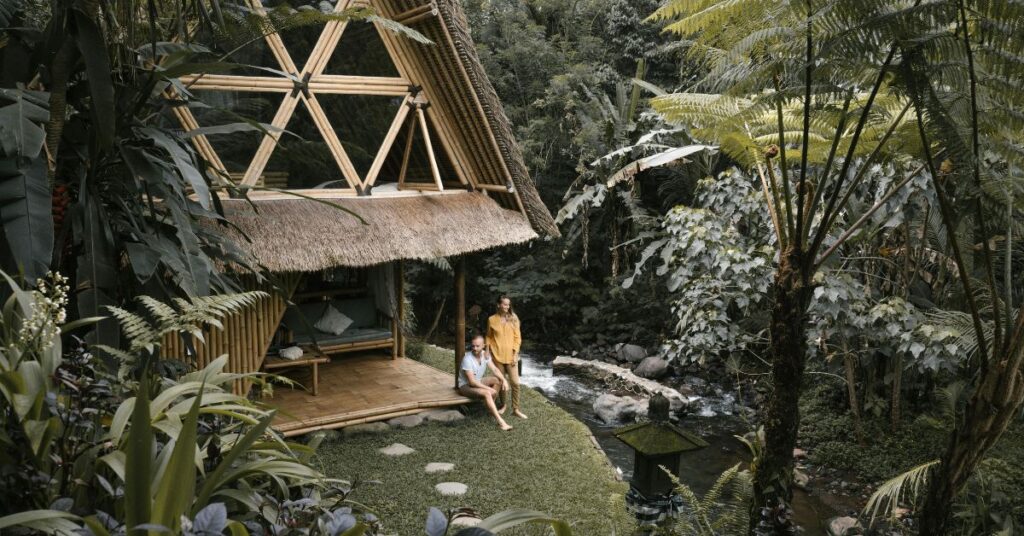 一对夫妇在巴厘岛丛林溪流边的竹子生态屋，展示可持续发展的海岛生活。