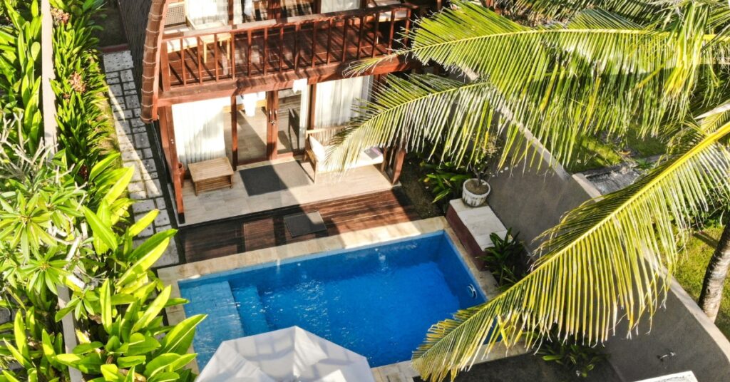 Hur man hyr en bali-villa. En villa med privat pool, träbalkong och lummig grönska, sedd uppifrån i varmt solljus.
