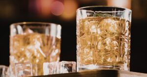 Gros plan sur une liqueur ambrée dans des verres remplis de glaçons, symbolisant les lois sur l'alcool, les recommandations de consommation, la culture de la boisson et la consommation responsable en Indonésie.