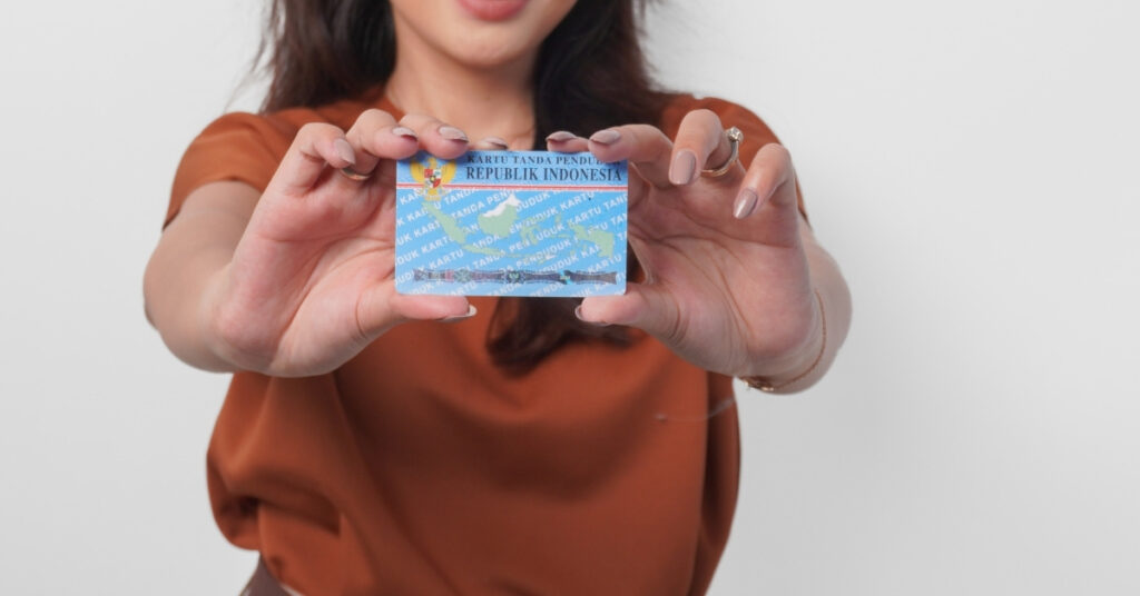 Carta d'identità indonesiana. Donna indonesiana che mostra la sua carta d'identità elettronica (e-ktp) verso la telecamera con entrambe le mani, in uno studio.