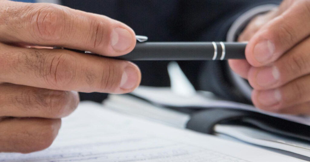 Primo piano di mani che tengono una penna su un modulo di richiesta di carta d'identità indonesiana, preparandosi a firmare documenti ufficiali.