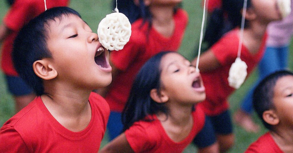 Niños con camisetas rojas compiten por comer galletas colgantes sin usar las manos durante un juego del Día de la Independencia de Indonesia.