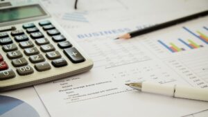 Une calculatrice, un stylo et des rapports financiers accompagnés de graphiques posés sur un bureau, illustrant les calculs relatifs à l'imposition et au paiement des impôts.
