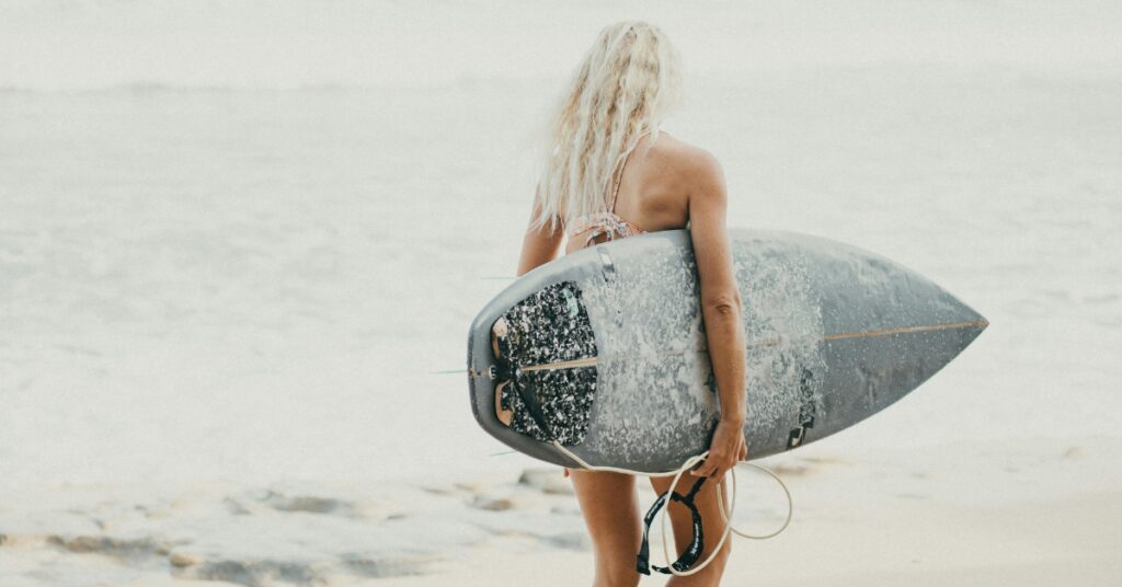 有効なビザで入国した観光客を代表して、サーフボードを持った女性がインドネシアのビーチに向かって歩く。