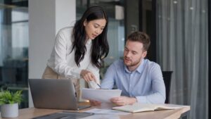 Een Indonesische medewerkster begeleidt een buitenlandse medewerker aan een bureau terwijl ze documenten doorneemt in het kader van de aanvraagprocedure voor een stagevisum.