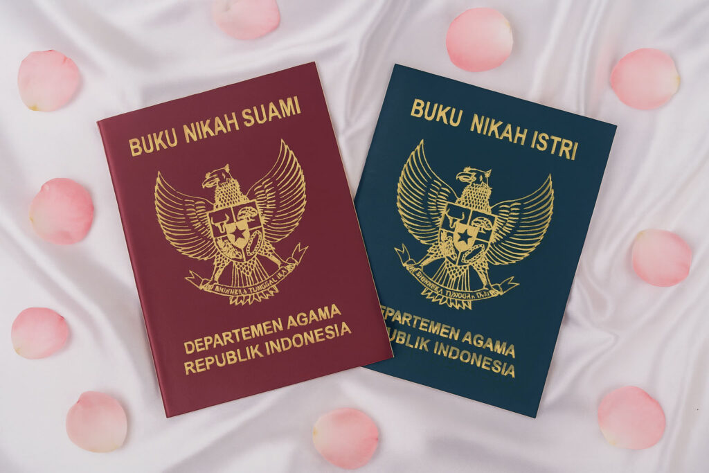 Indonesian marriage books for husband and wife issued by the ministry of religious affairs, placed on white satin cloth with pink rose petals.