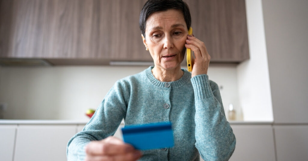 Жінка, яка тримає кредитну картку під час телефонної розмови, виглядає стурбованою можливим шахрайством або прихованими комісіями під час обміну грошей.