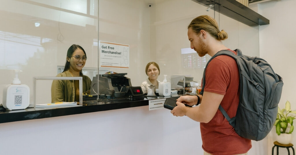 Турист біля стійки обміну валюти в Балі, де за склом усміхнені працівники готуються обміняти іноземну валюту.
